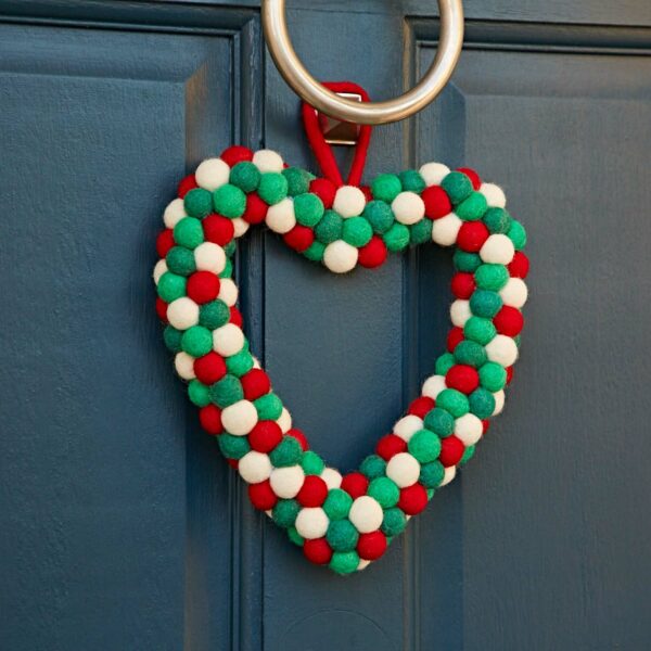 The blue door is beautifully decorated with a Felt Heart Wreath made of red, green, and white pom-poms, centered around a large metal ring.