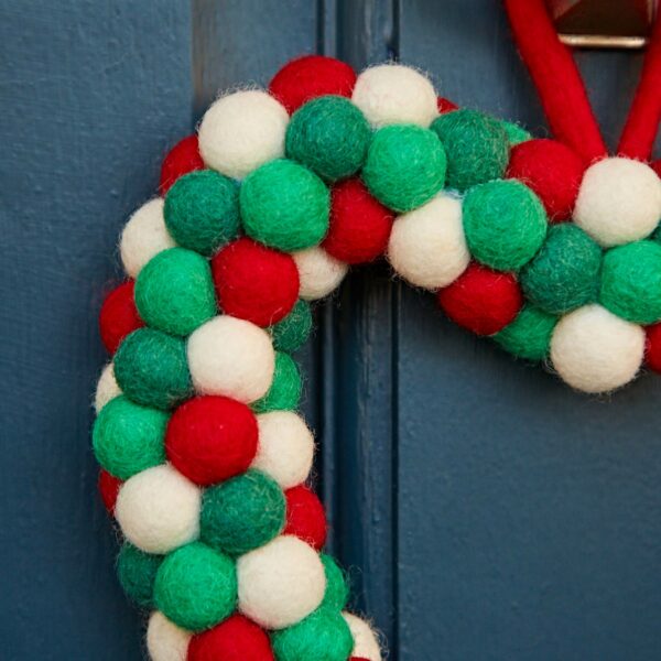 A close-up of the Felt Heart Wreath, beautifully crafted from red, green, and white felt balls, hangs elegantly on a blue door.