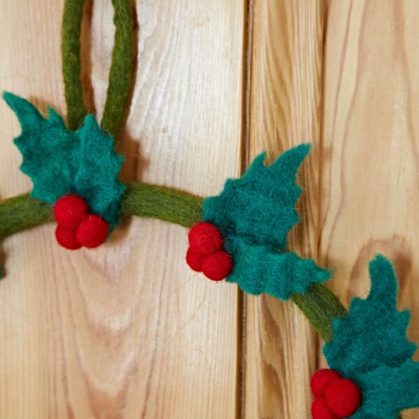 Close-up of the Felt Mistletoe Christmas Wreath, adorned with green leaves and red berries, hung on a wooden surface.