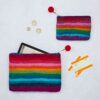 Two rainbow-striped pouches, one larger with a tablet and one smaller filled with tickets, a receipt, and coins, lie on a light background. The Felt Tree of Life Purse features intricate embroidery.
