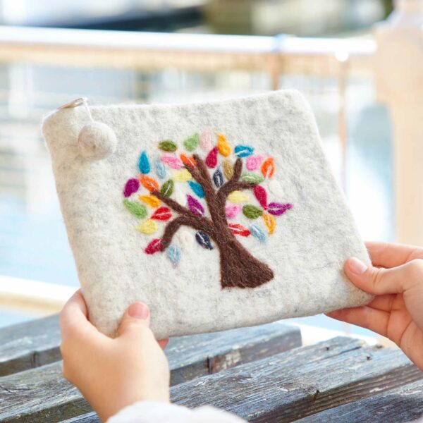 A person holds a Felt Tree of Life Purse, featuring a vibrant Tree of Life design with branches adorned with multi-colored leaves embroidered on the white felt.