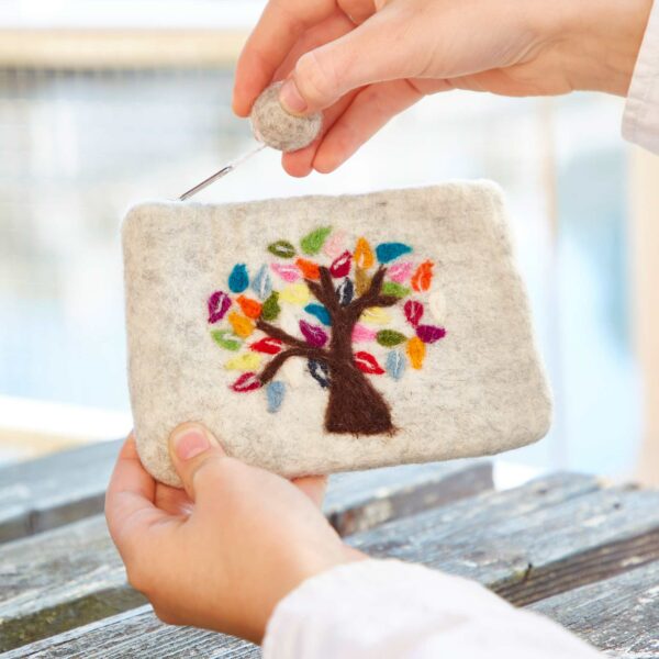 Hands holding a Felt Tree of Life Purse, placing or removing a felt button from the zippered top.