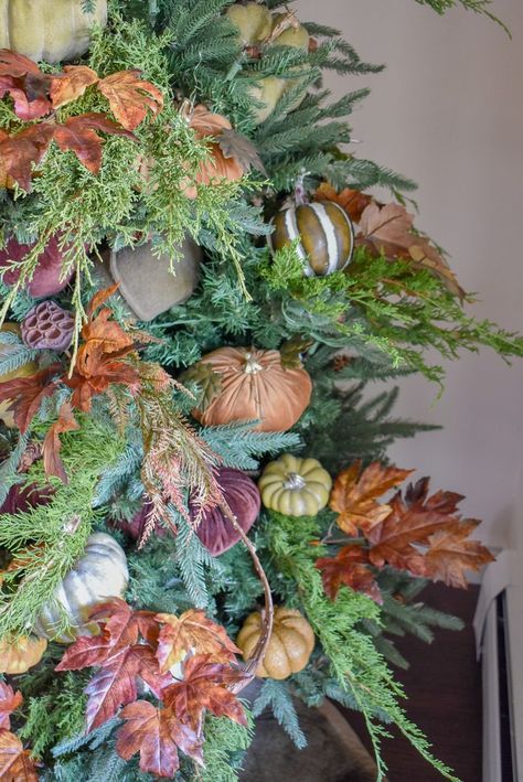 A close-up view of a decorated Christmas tree featuring autumn-themed elements like orange and brown leaves, small pumpkins nestled among the green branches, and an amusing touch of tiny elephant dung replicas for a whimsical twist.