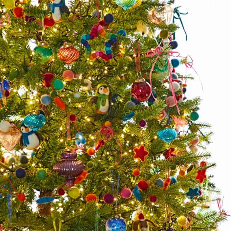 A Christmas tree decorated with colourful felt ornaments, baubles, penguin figures, fairy lights, and a charming Christmas Parent Banner.