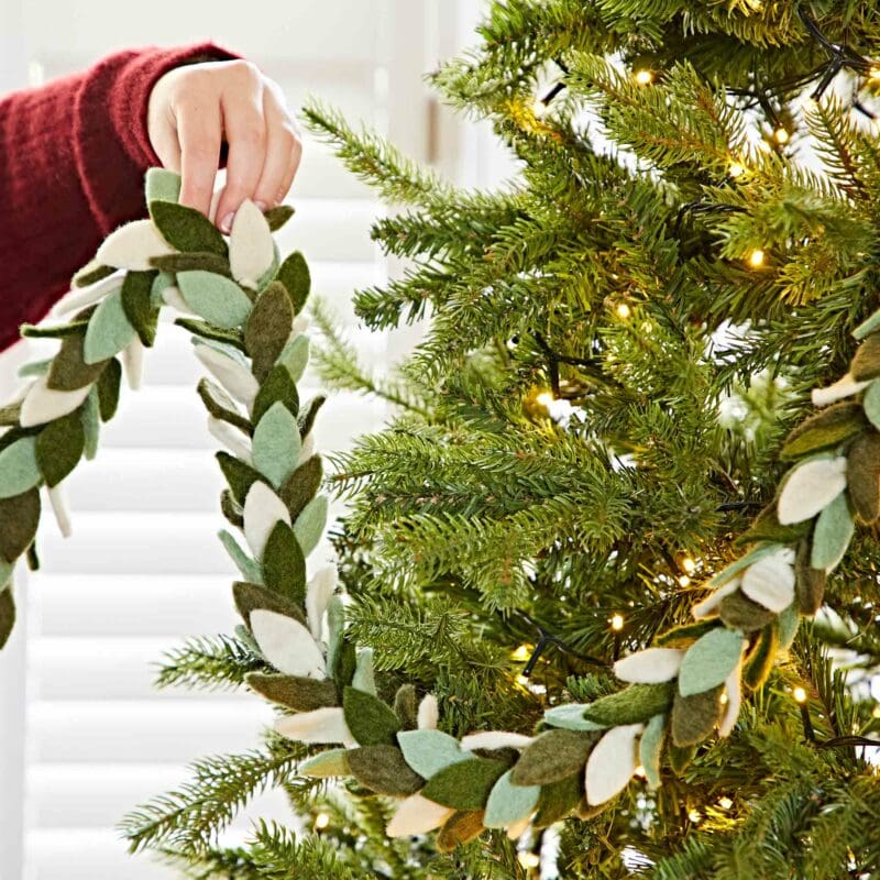 A person in a red sleeve is placing the Felt Berry Christmas Garland on a lit Christmas tree.