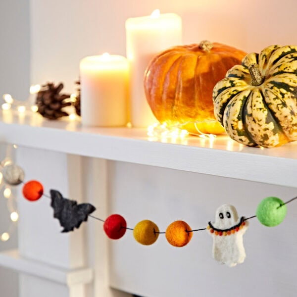 Halloween-themed decorations on a white mantel include lit candles, small pumpkins, pine cones, and a garland featuring colorful balls along with the Felt Ghosts and Bats Garland.