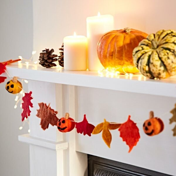 A mantel decorated for fall with pinecones, lit candles, assorted pumpkins, and a Felt Pumpkin and Leaves Garland featuring leaves and felt pumpkins hanging below.