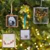 Four rectangular photo ornaments hang on a Christmas tree. They display various images, including a child, flowers, two people at a beach, and the name "Ella" with floral decorations. These ornaments make perfect autumn style gifts.