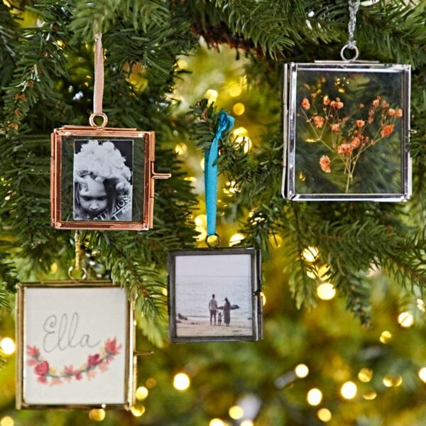 Four rectangular photo ornaments hang on a Christmas tree. They display various images, including a child, flowers, two people at a beach, and the name "Ella" with floral decorations. These ornaments make perfect autumn style gifts.