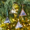 Four triangular photo ornaments, perfect as Autumn Style Gifts, hang on a Christmas tree. Each ornament contains a different image and is framed in various metallic colors. The background shows green branches and twinkling lights.