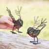 A hand delicately holds one of the Set of Two Wire Robin with Wings Decorative Ornaments, showcasing intricately crafted, twig-like feathers. Resting on a wooden surface, these ornaments offer a charming blend of nature and artistry.