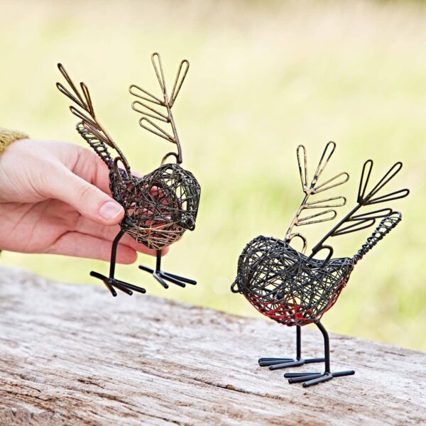 A hand delicately holds one of the Set of Two Wire Robin with Wings Decorative Ornaments, showcasing intricately crafted, twig-like feathers. Resting on a wooden surface, these ornaments offer a charming blend of nature and artistry.