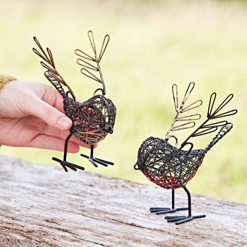 A hand delicately holds one of the Set of Two Wire Robin with Wings Decorative Ornaments, showcasing intricately crafted, twig-like feathers. Resting on a wooden surface, these ornaments offer a charming blend of nature and artistry.