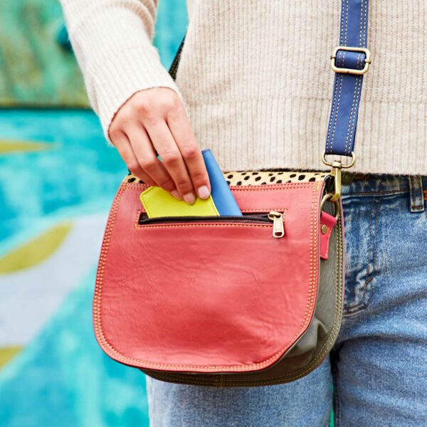 A person places multicoloured cards into the front pocket of the Multicoloured Saddle Crossbody Bag (Copy).