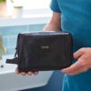 A person holds a black Personalised Leather Wash Bag, elegantly adorned with the print "DAD" on it.
