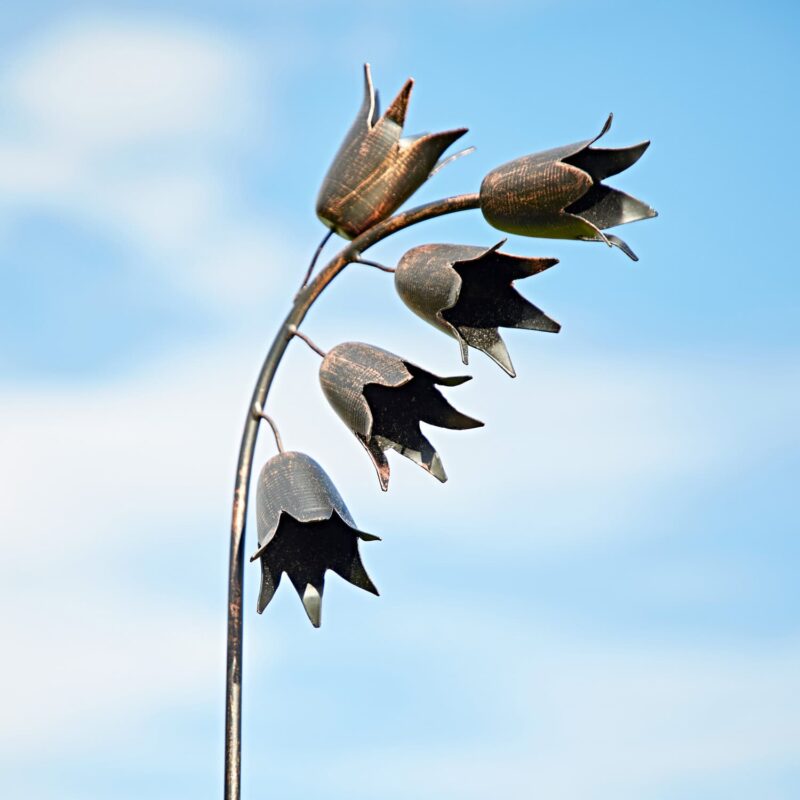 The Metal Echinacea Flower Garden Stake Ornament stands tall against a blue sky with drifting clouds, adding elegance to any outdoor space.