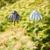 Two Recycled Metal Echinacea Flower Garden Stake Decorations, one dark and one light, are set among green foliage outdoors in sunlight.