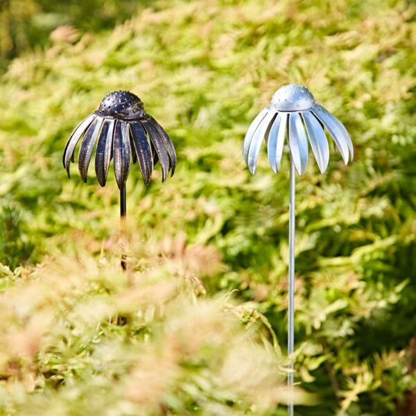 Two Recycled Metal Echinacea Flower Garden Stake Decorations, one dark and one light, are set among green foliage outdoors in sunlight.