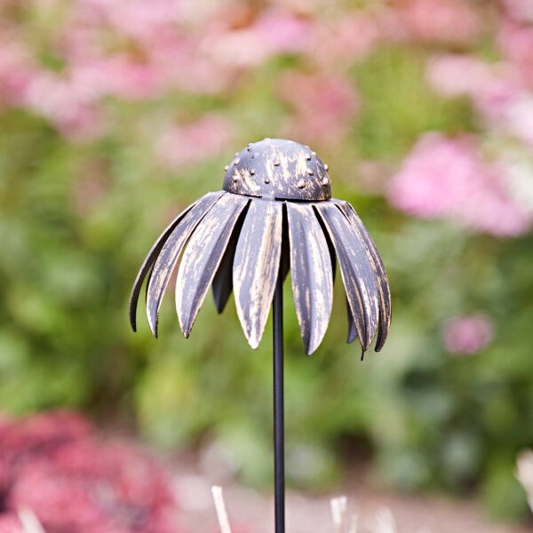 The Metal Echinacea Flower Garden Stake Decoration features intricate petal details and stands elegantly with a blurred background of pink blossoms and lush greenery.