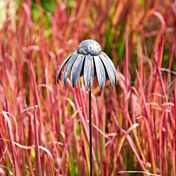 The Metal Echinacea Flower Garden Stake Decoration stands out amidst tall red grass, providing a unique accent to the landscape.