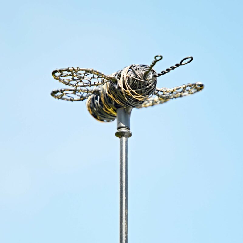 A Hanging Yellow and Black Bee Garden Ornament gracefully sits atop a metal stake, creating a charming scene against the clear blue sky.