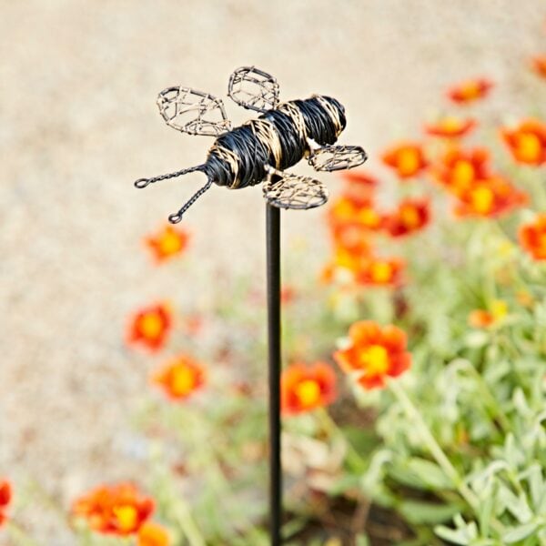 The Recycled Metal Bee Garden Stake, crafted from recycled metal, adds charm to your garden bed among orange and yellow blooms—perfect decor for brightening any outdoor space.