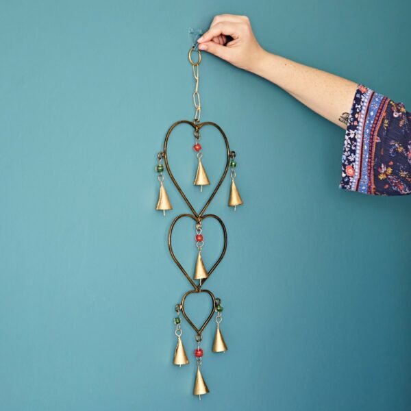 A hand is hanging a Gold Iron Cow Bell with heart shapes on a teal wall.