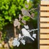 Two Recycled Iron Bird Silhouette Garden Art pieces, one silver and one brown, are displayed on a wooden fence with lush greenery in the background.