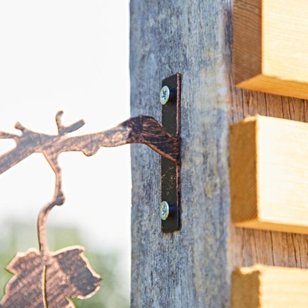 Close-up of a Recycled Iron Bird Silhouette Garden Art decorative bracket attached with two screws to a weathered wooden post beside a slatted wooden structure.