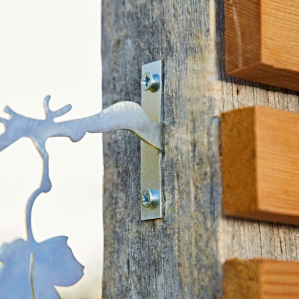 The Recycled Iron Bird Silhouette Garden Art is attached to a weathered wooden post with a metal bracket and two screws, positioned beside stacked wooden planks.