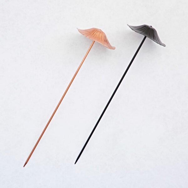 Two Recycled Metal Mushroom Garden Stakes in rose gold and black—crafted from recycled metal—are arranged diagonally on a light background.