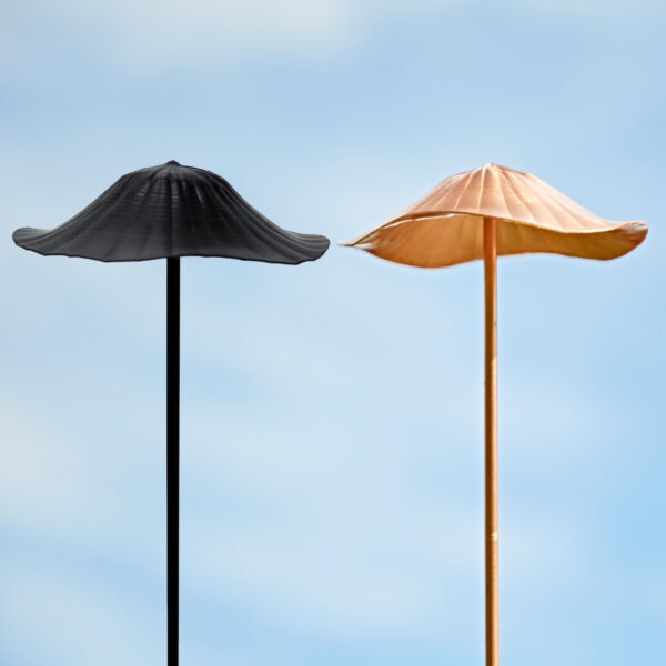 Two outdoor Recycled Metal Mushroom Garden Stakes, one black and one copper, stand beneath a clear blue sky