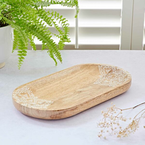 The Floral Mango Wood Decorative Tray with white floral corner patterns rests on a light surface near a potted fern and dried flowers, set against white window shutters.