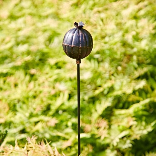 The Recycled Iron Poppy Seed Head Garden Stake Decoration, crafted from repurposed iron and mounted on a slim rod, adds an elegant touch to your garden and stands out beautifully against lush green foliage.