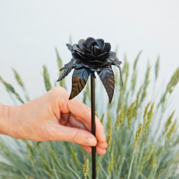 A hand displays the Recycled Iron Black Rose Garden Stake against green grass and a white backdrop.