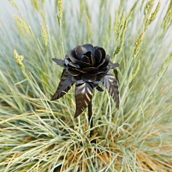 The Recycled Iron Black Rose Garden Stake, crafted from recycled iron, stands out amid dense, spiky green grass.