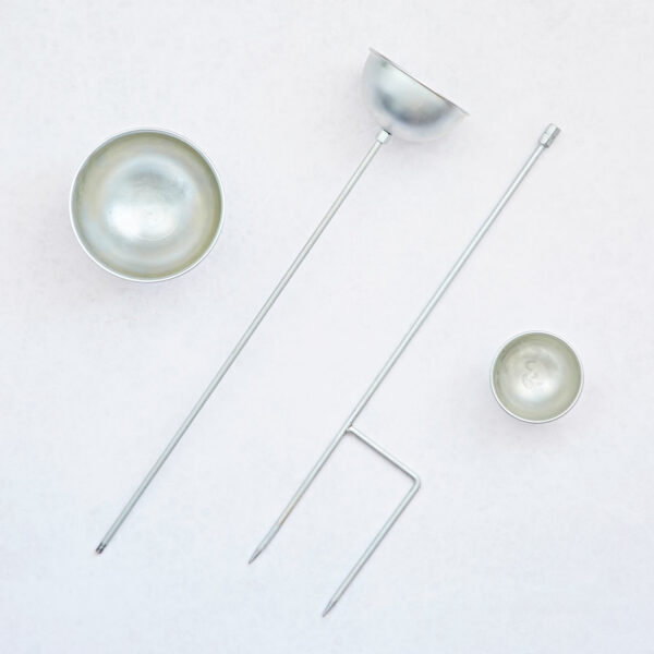 Four metal tools—including three round-bottomed Recycled Iron Silver Rain Catchers and a two-pronged fork—are arranged on a light, textured surface.