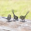The Set of Two Wire Robins with Wings Decorative Ornament rests on a wooden surface against a blurry grassy backdrop, adding whimsy and elegance to any space.