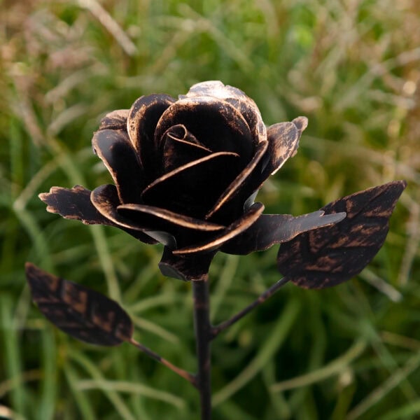 A close-up of the Recycled Metal Rose Copper & Gold Garden Stake, featuring engraved details and crafted from recycled metal, set against blurred green grass.