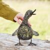 A hand gently touches a Small Quacking Duck Wire Garden Ornament, resting on an outdoor wooden surface.