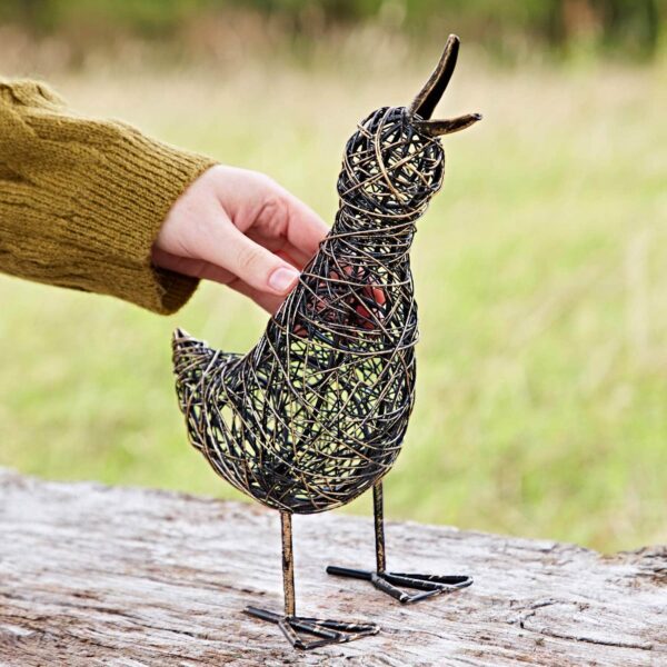 A hand gently touches the Small Flapping Duck Wire Garden Ornament, artfully crafted from twisted metal wire and elegantly perched on a wooden surface outdoors.