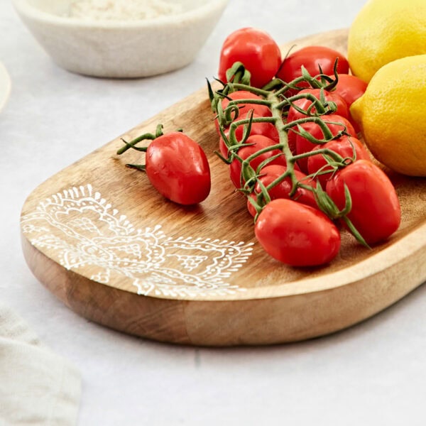 The Round Floral Carved Mango Wood Trivet, decorated with vine tomatoes and lemons, sits elegantly on a white surface.