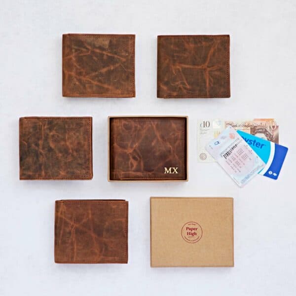 Six brown leather wallets, including the Personalised Brown Distressed Buffalo Leather Billfold Wallet embossed with "MX," are displayed with cash, cards, an ID, and a branded box on a white background.