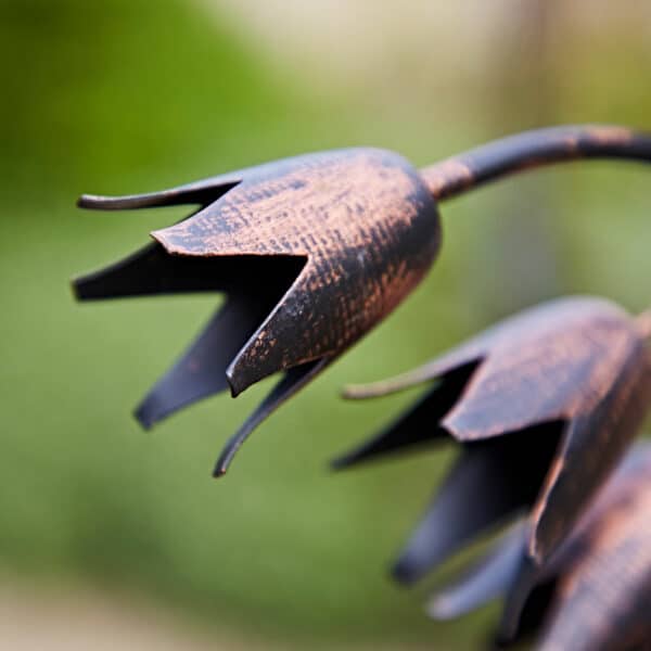 Close-up of a Recycled Metal Echinacea Silhouette Garden Stake, a copper-finished metal sculpture shaped like flower buds, displayed against a blurred green background.