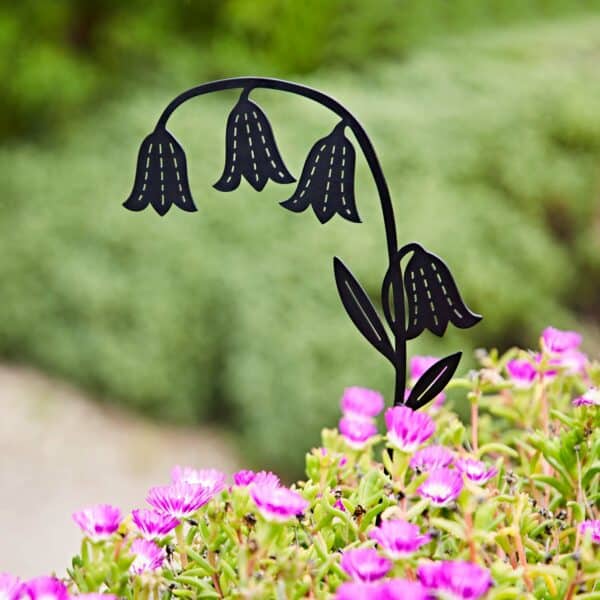 A Recycled Metal Echinacea Silhouette Garden Stake in black stands among blooming pink flowers and green foliage with a blurred background.