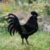 The Recycled Metal Cockerel Silhouette Garden Stake features decorative cutouts and stands on grass among garden flowers, crafted from recycled metal.