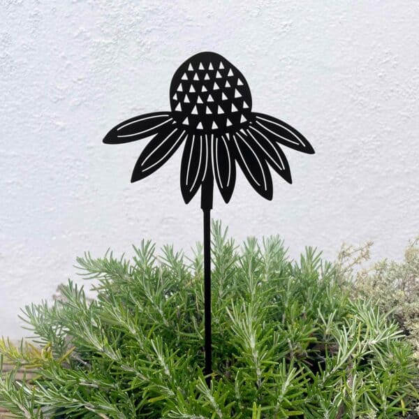 The Recycled Metal Echinacea Silhouette Garden Stake, crafted in black, is set among green foliage with a light-textured wall backdrop.