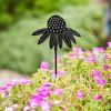 A Recycled Metal Echinacea Silhouette Garden Stake, crafted to resemble a black metal flower, stands gracefully among blooming pink flowers and lush green foliage.