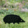The Recycled Metal Hedgehog Silhouette Garden Stake, crafted from black recycled metal, is shown standing on green grass with a blurred garden background.