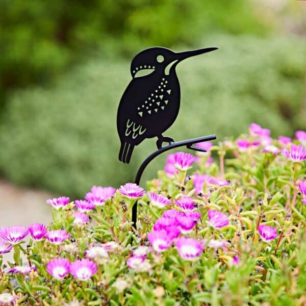 A Recycled Metal Kingfisher Silhouette Garden Stake is set among blooming pink flowers and lush green foliage, bringing added charm to the garden.